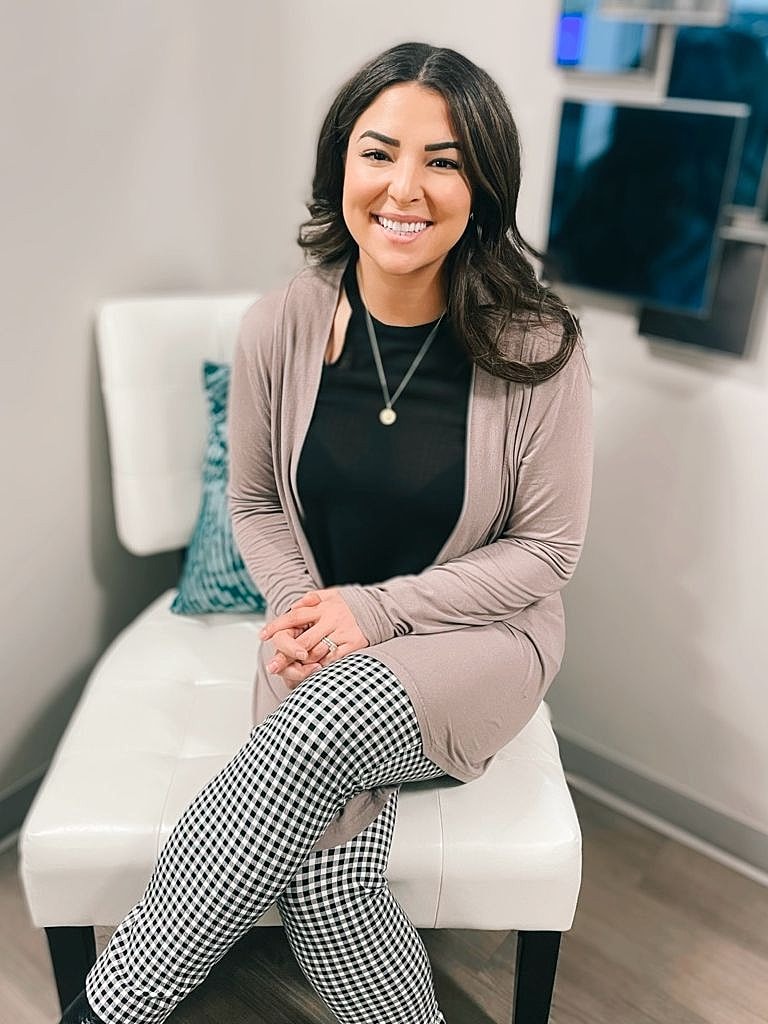 Woman smiling while seated on a white chair.