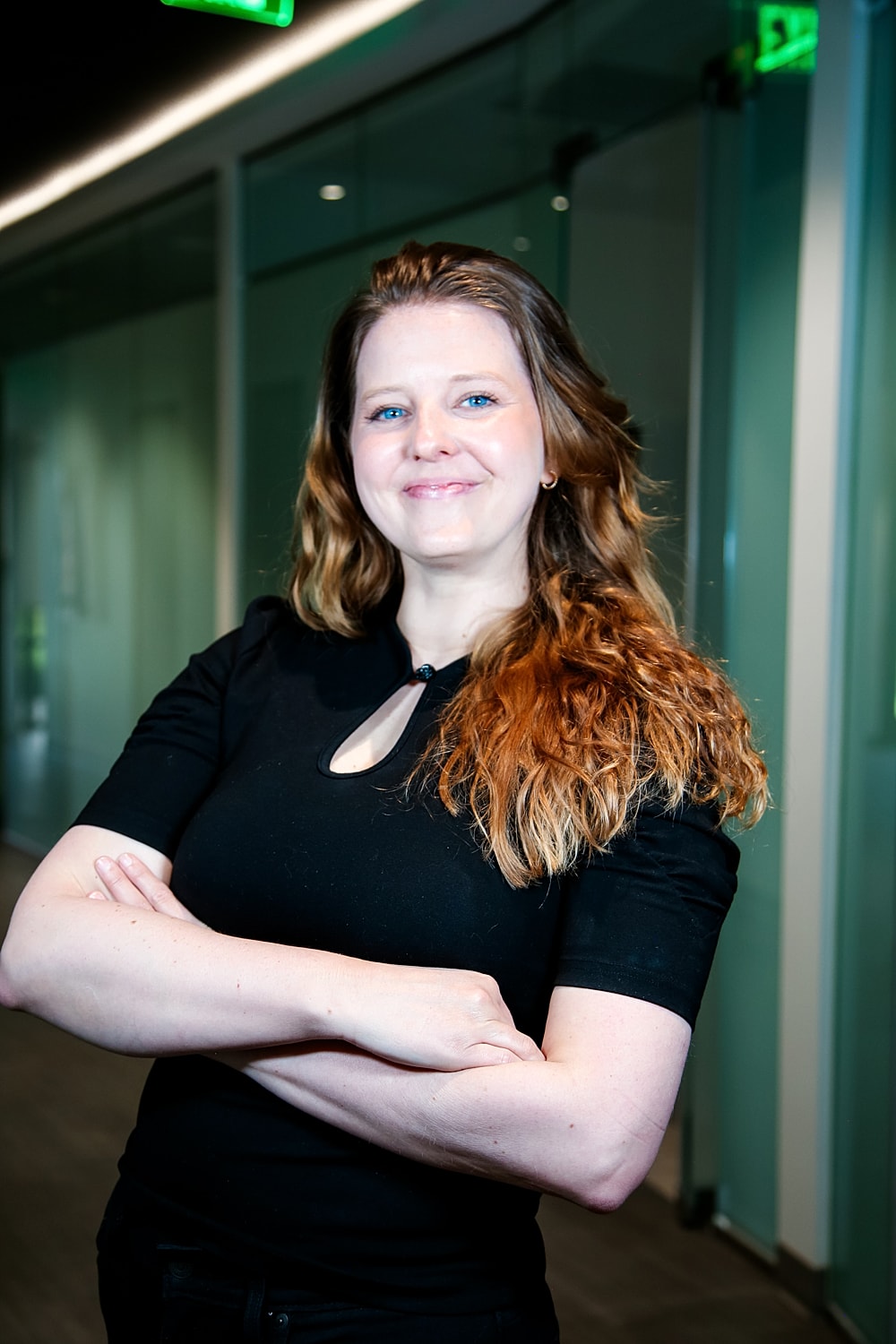Smiling woman standing with arms crossed indoors.