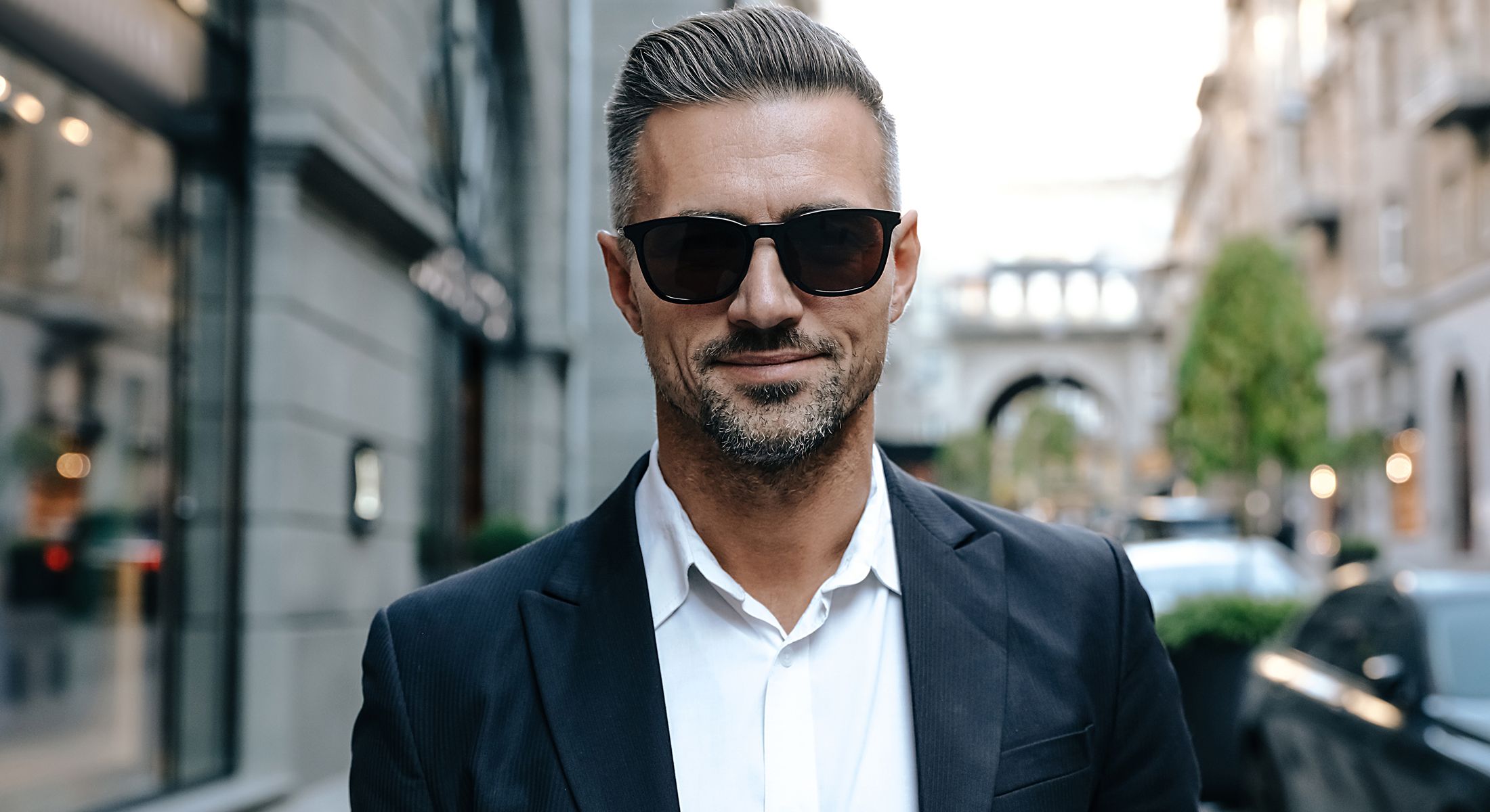 Man in suit and sunglasses on city street.