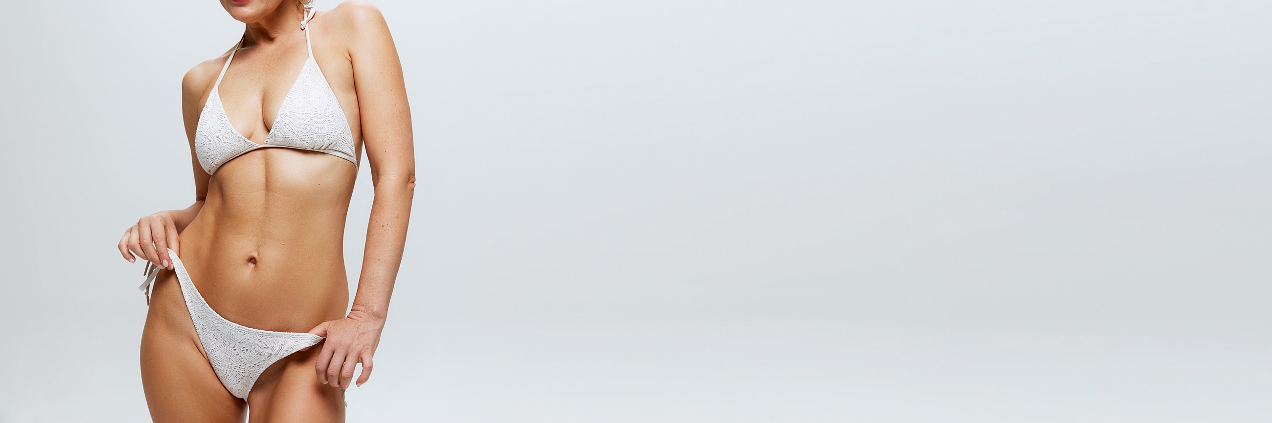 Model in white bikini against gray background.