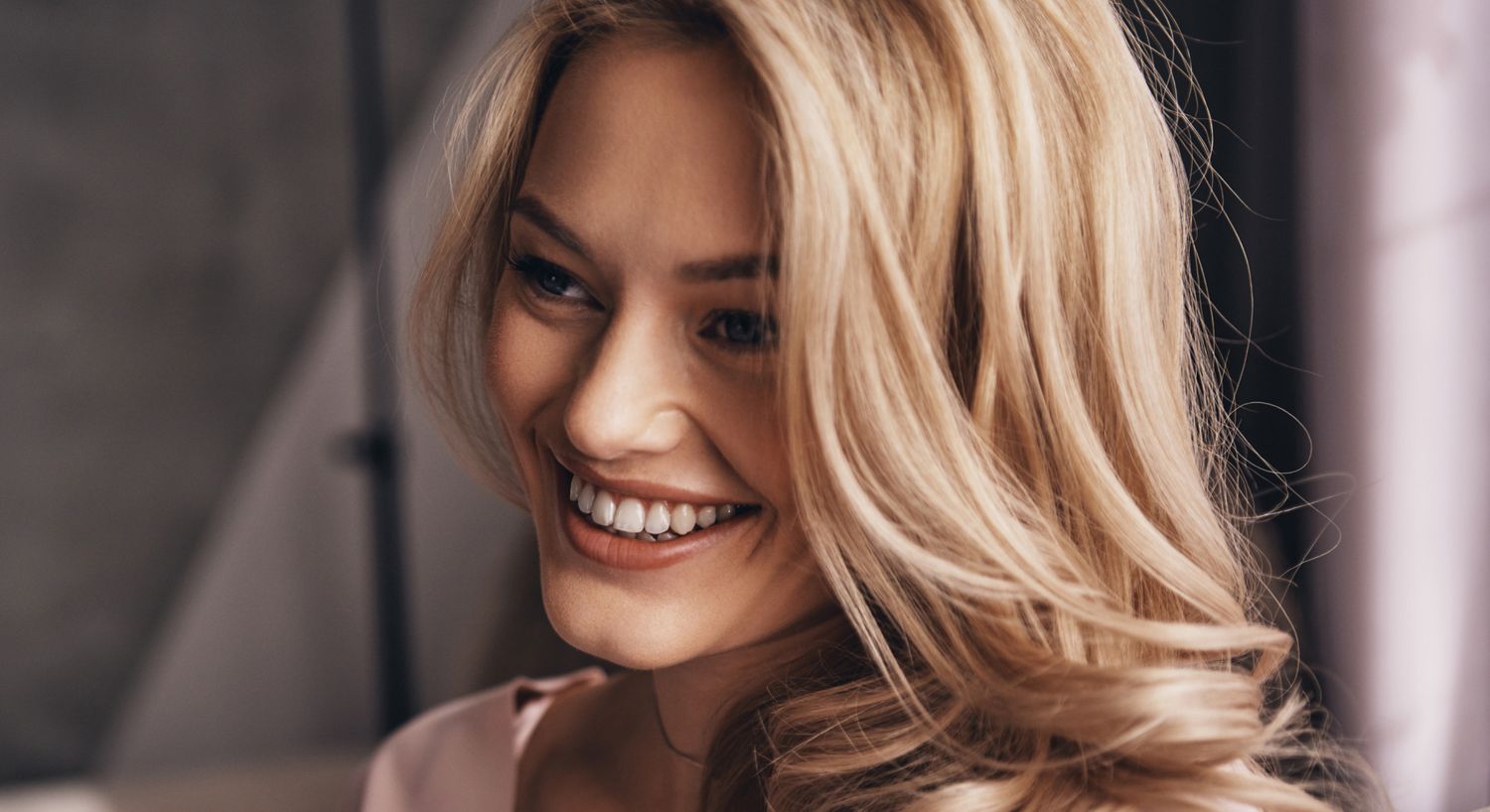 Smiling woman with blonde hair in soft lighting.