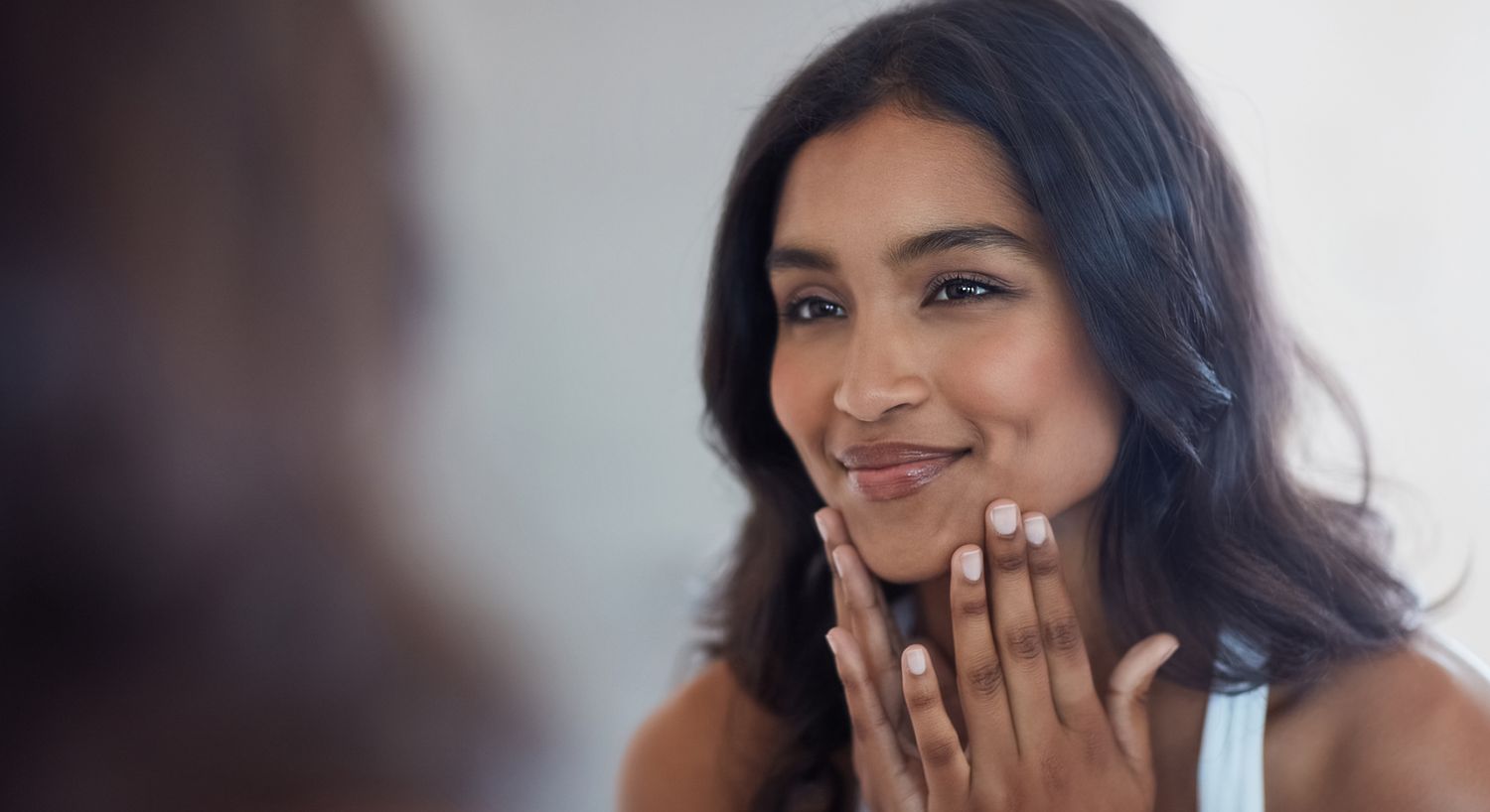 Woman smiling while touching her face in mirror.